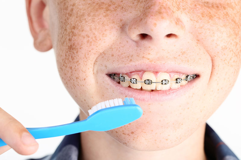 closeup of a boy with freckles holding a toothbrush by his mouth
